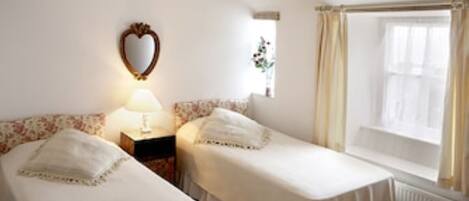 A room with two single beds, a nightstand with a lamp, a mirror, and a window with curtains.