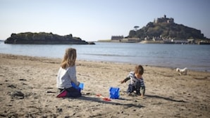 Two children playing on a sandy beach with a castle-like structure in the background.