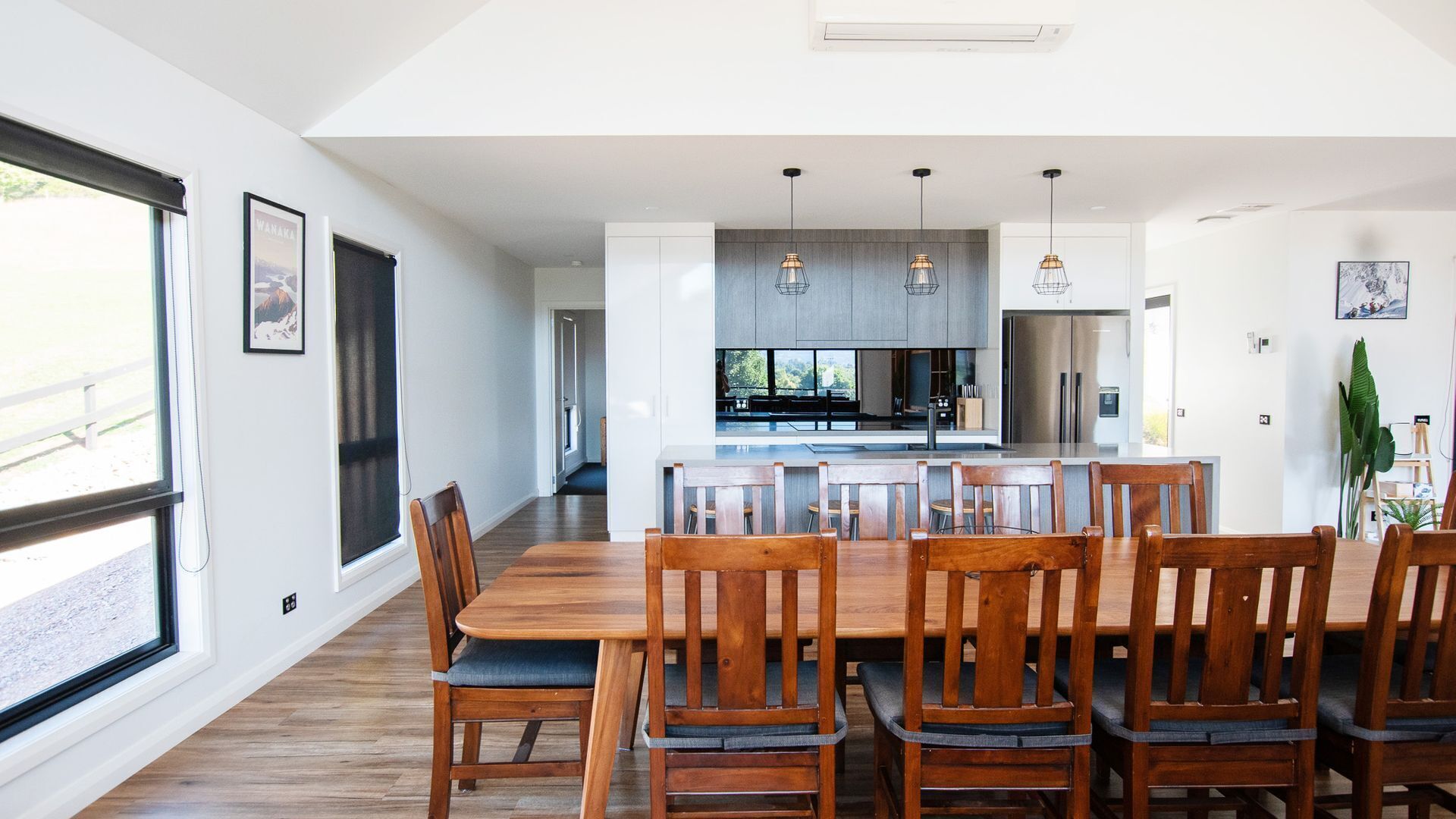 Une cuisine moderne dotée d’un îlot central, de luminaires suspendus et d’un coin repas avec des chaises en bois et une grande table.
