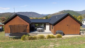 Une maison moderne à deux étages dotée d’un patio couvert, d’un trampoline et d’un barbecue.