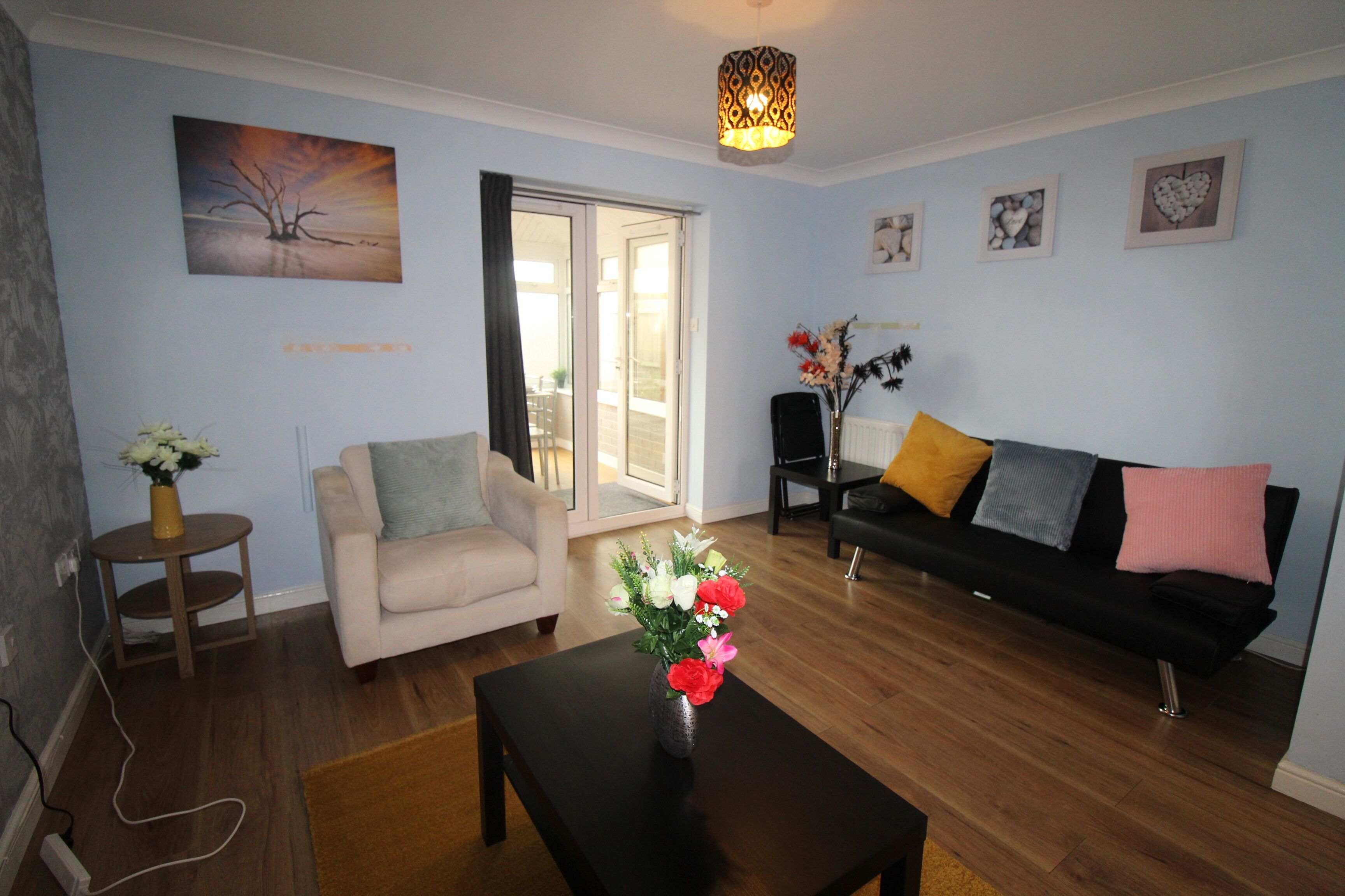 A living room with a sofa, armchair, coffee table, and a vase of flowers.