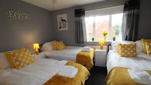 A hotel room with two beds, each with a yellow bedspread and white bedding. There is a window with curtains, a bedside table with a lamp, and a wall decoration that reads "LOVE". - Harriers Grove House (Sutton-in-Ashfield)