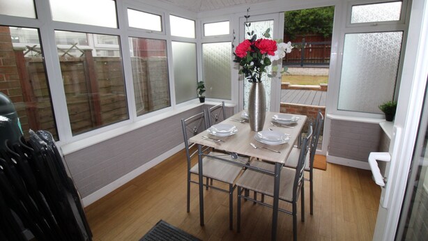 A dining area with a table set for four, a vase with flowers, and a view of the outside. - Harriers Grove House (Sutton-in-Ashfield)