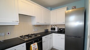 A kitchen with white cabinets, a stainless steel refrigerator, a microwave, and a gas stove. - Harriers Grove House (Sutton-in-Ashfield)
