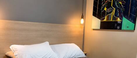 A neatly made bed with white and dark bedding, a wooden headboard, and a modern light fixture.