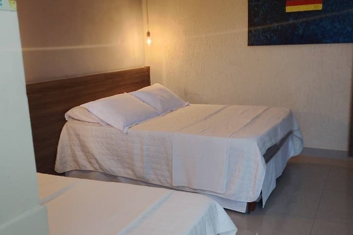 Une chambre d’hôtel avec deux lits, une tête de lit en bois, une lampe fixée au mur et un petit tableau.