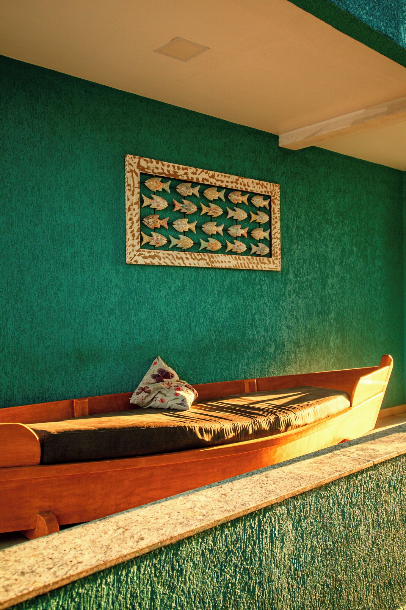 A room with a green textured wall, a wooden bench with cushions, and a framed artwork above the bench.