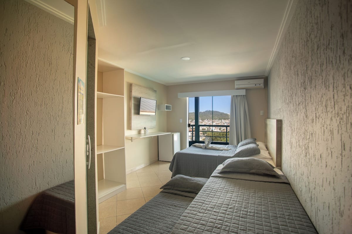 Une chambre d’hôtel avec deux lits, un petit bureau, une télévision et un balcon avec vue.