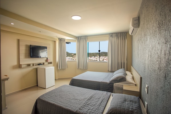 A hotel room with two beds, a TV, a small fridge, and a window with curtains.
