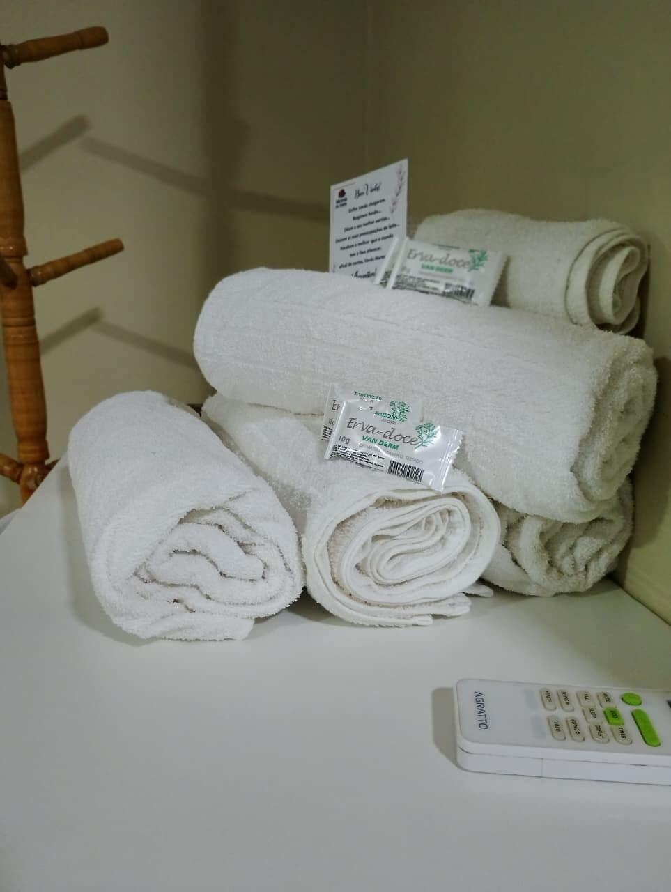Uma pilha de toalhas brancas com etiquetas, um controle remoto e uma cadeira de madeira em um quarto.