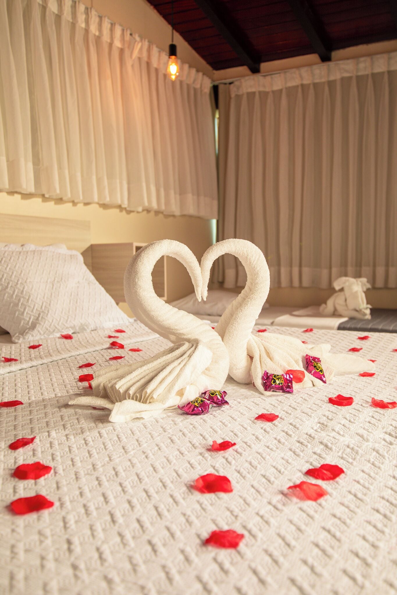A bed with a heart-shaped towel arrangement and rose petals.
