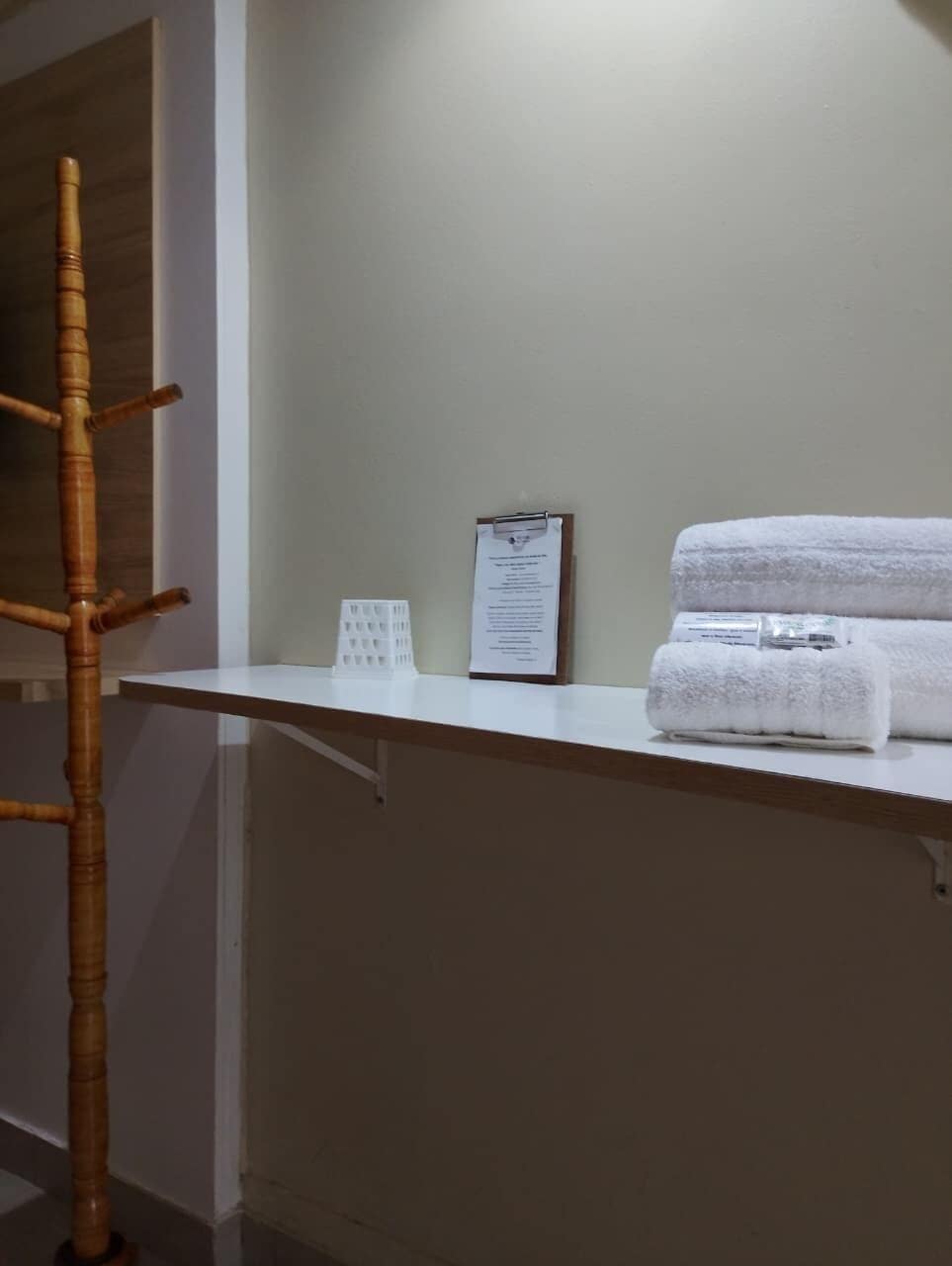 A white shelf with a clipboard, a white towel, and a bamboo chair.