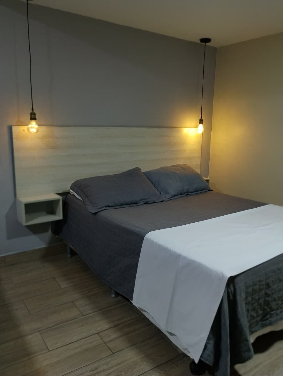 A bedroom with a bed, bedside tables, and hanging light fixtures.