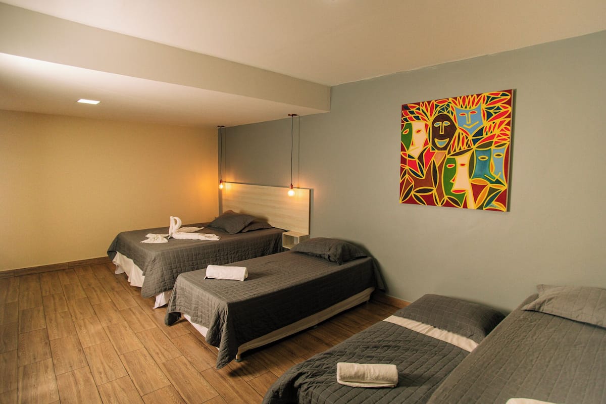 Une chambre d’hôtel avec deux lits simples, un grand lit et un tableau abstrait aux couleurs vives accroché au mur.