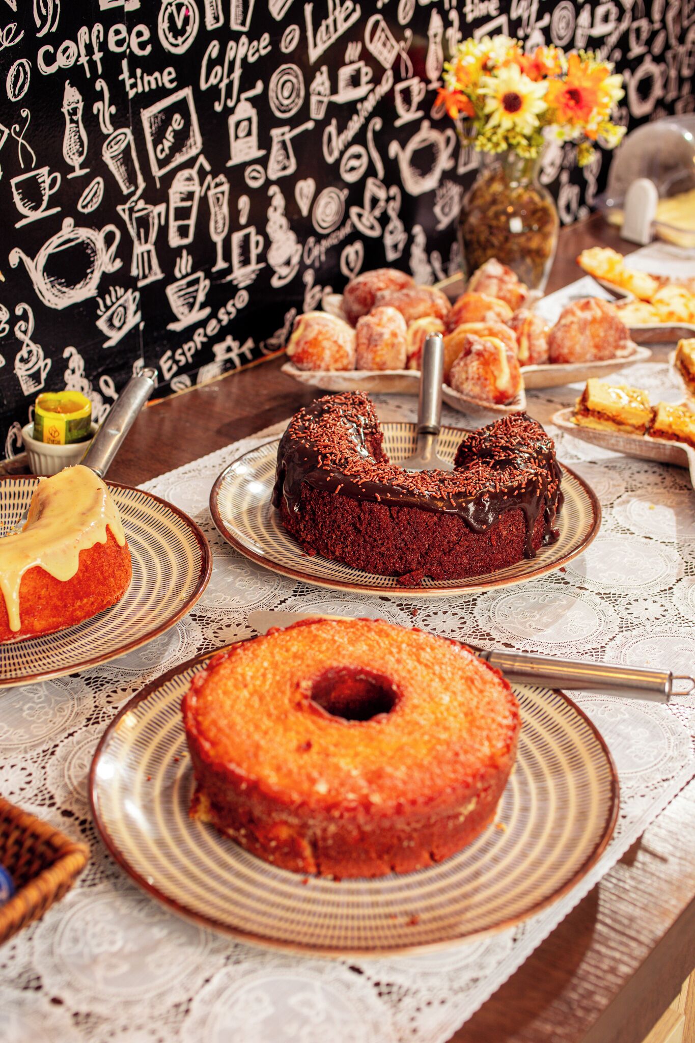 Una mesa con varios pasteles y dulces, una taza de café y un jarrón con flores.