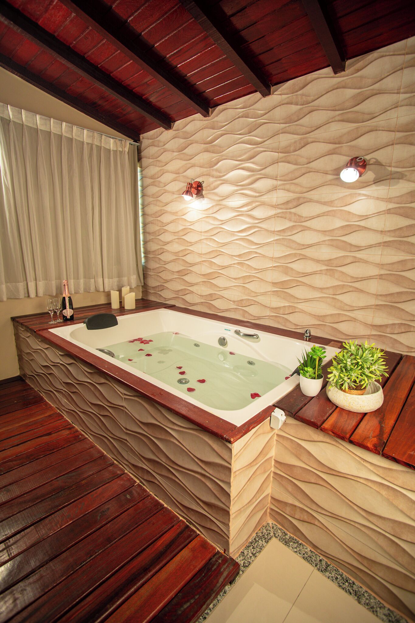 Un baño moderno con una bañera grande, suelo de madera, pared con textura y una planta en maceta a un lado.