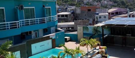 Un área de piscina en la azotea con sillones de descanso, un paraguas amarillo y vistas a un pueblo en la colina.