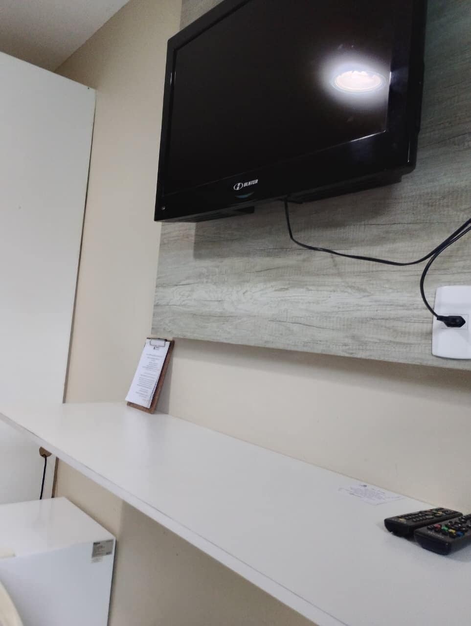 A flat-screen TV mounted on a wall with a wooden panel design, a white reception desk, and a remote control on the desk.