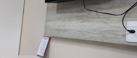 A flat-screen TV mounted on a wall with a wooden panel design, a white reception desk, and a remote control on the desk.