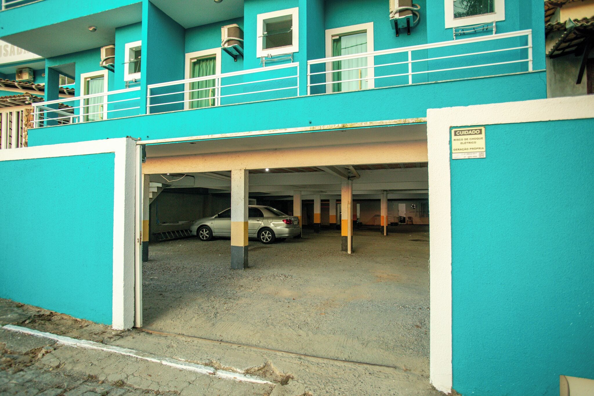 Een turquoise gebouw met een overdekte parkeerplaats en een auto.