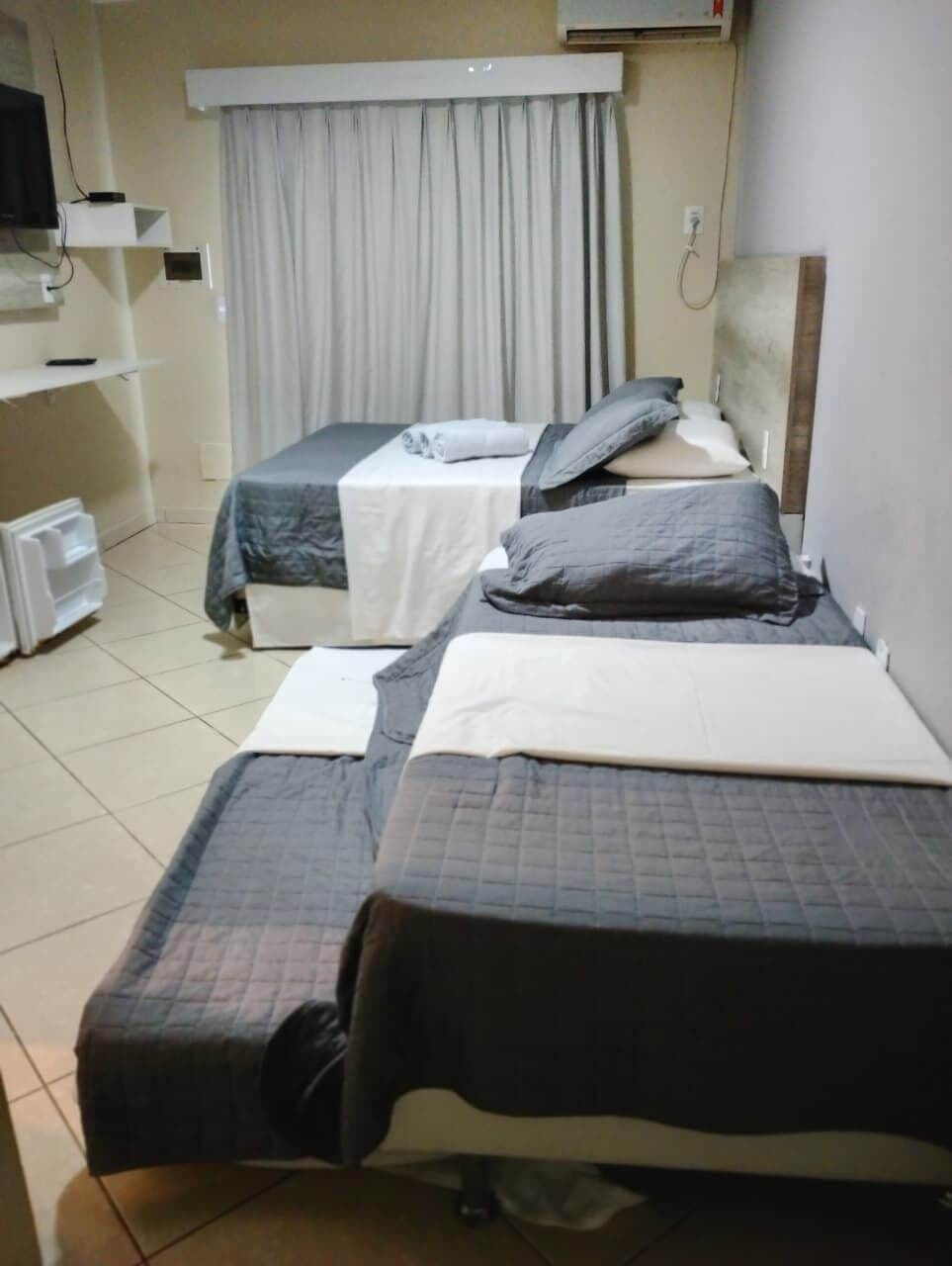 Une chambre d’hôtel avec deux lits, une télévision, une petite table et une fenêtre avec des rideaux.