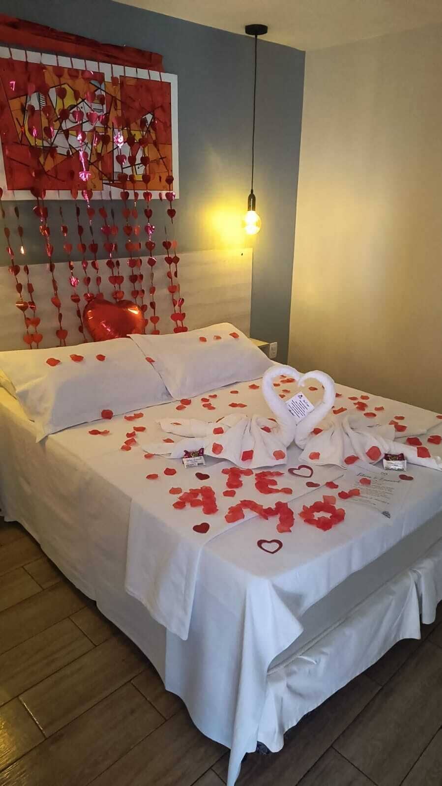 Quarto de hotel com uma cama, uma obra de arte na parede e um adorno pendurado.