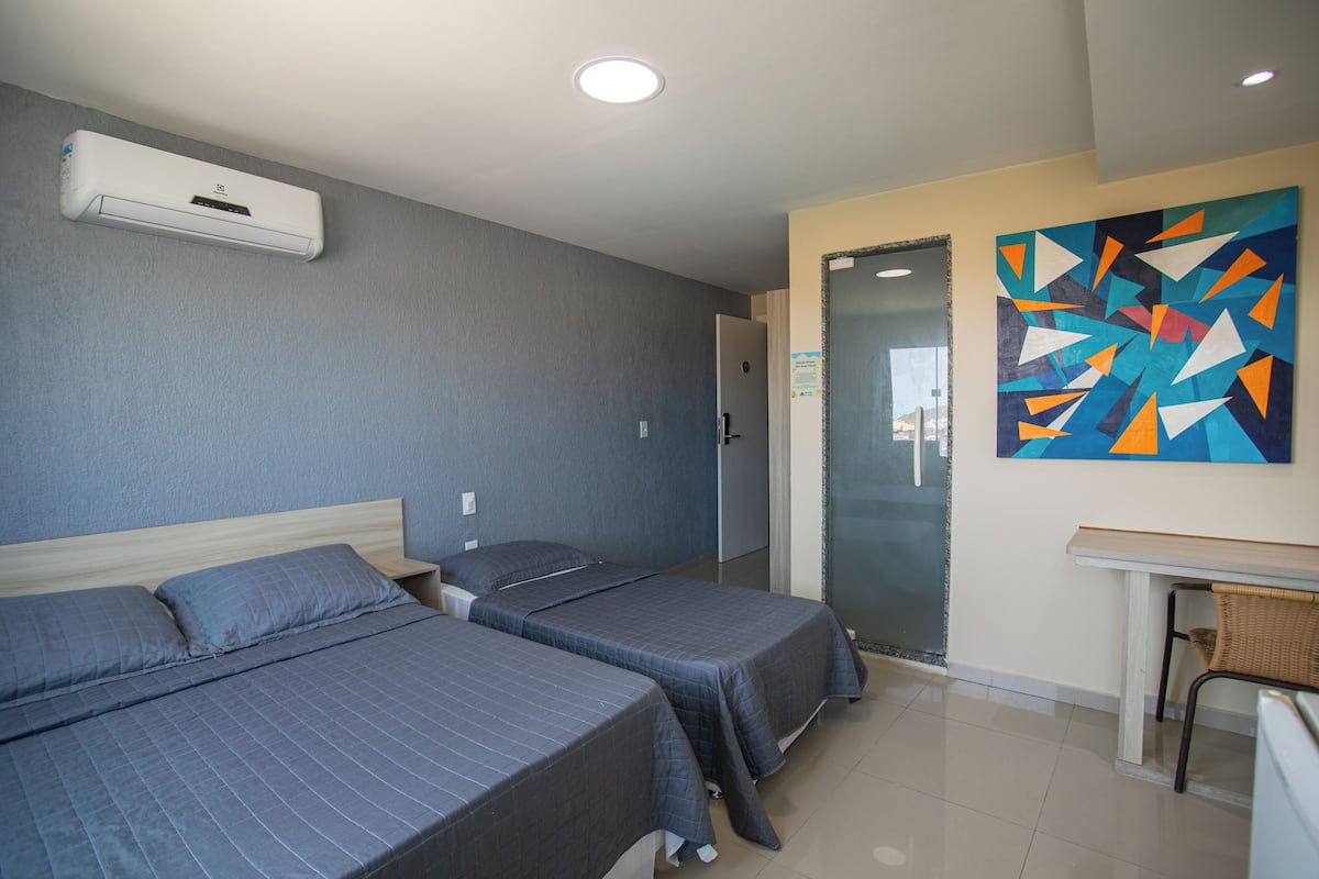 Une chambre d’hôtel avec deux lits, un bureau et une peinture abstraite aux couleurs vives accrochée au mur.