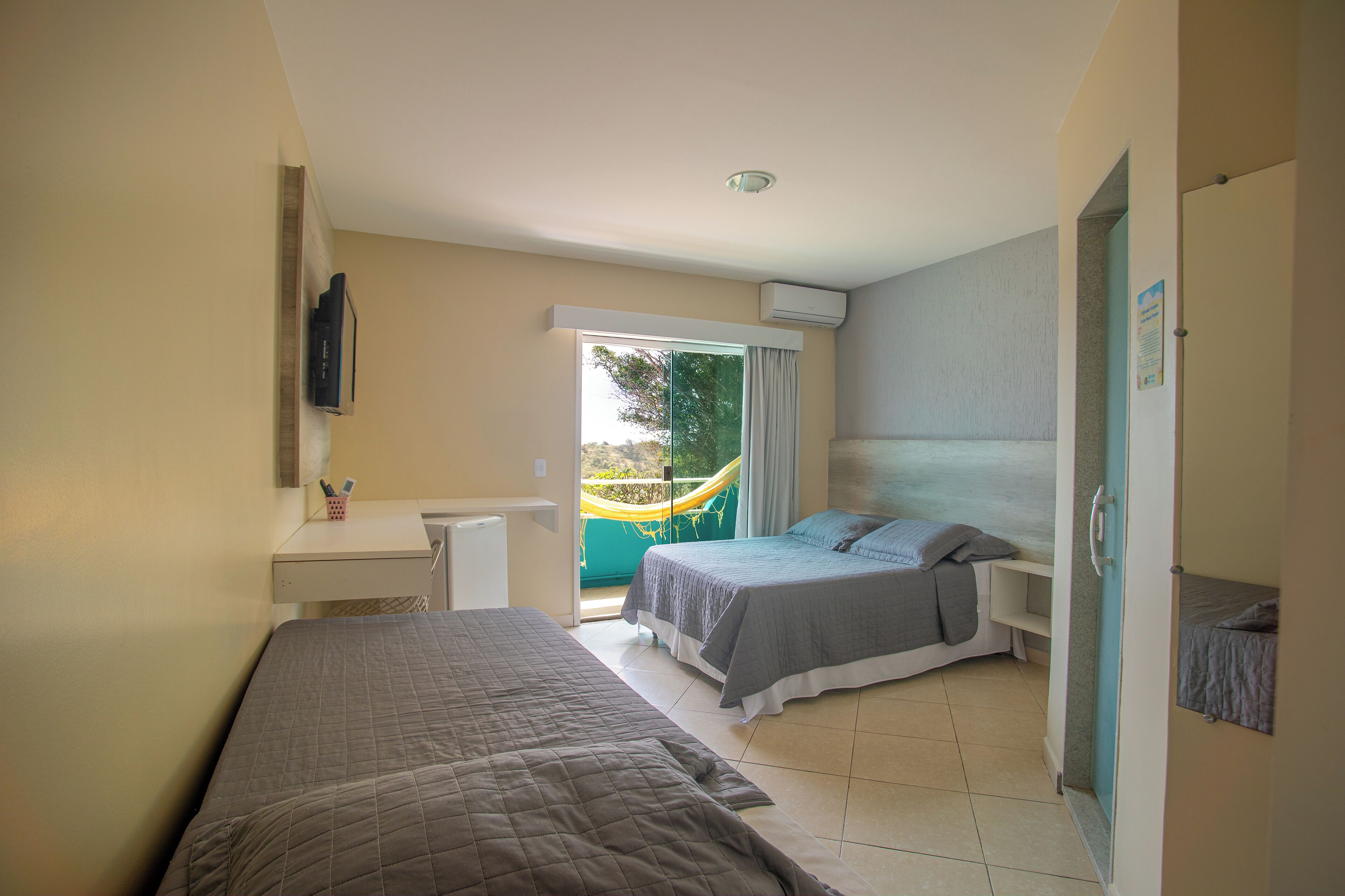 A bedroom with two beds, a desk, and a window with a view of a hammock outside.