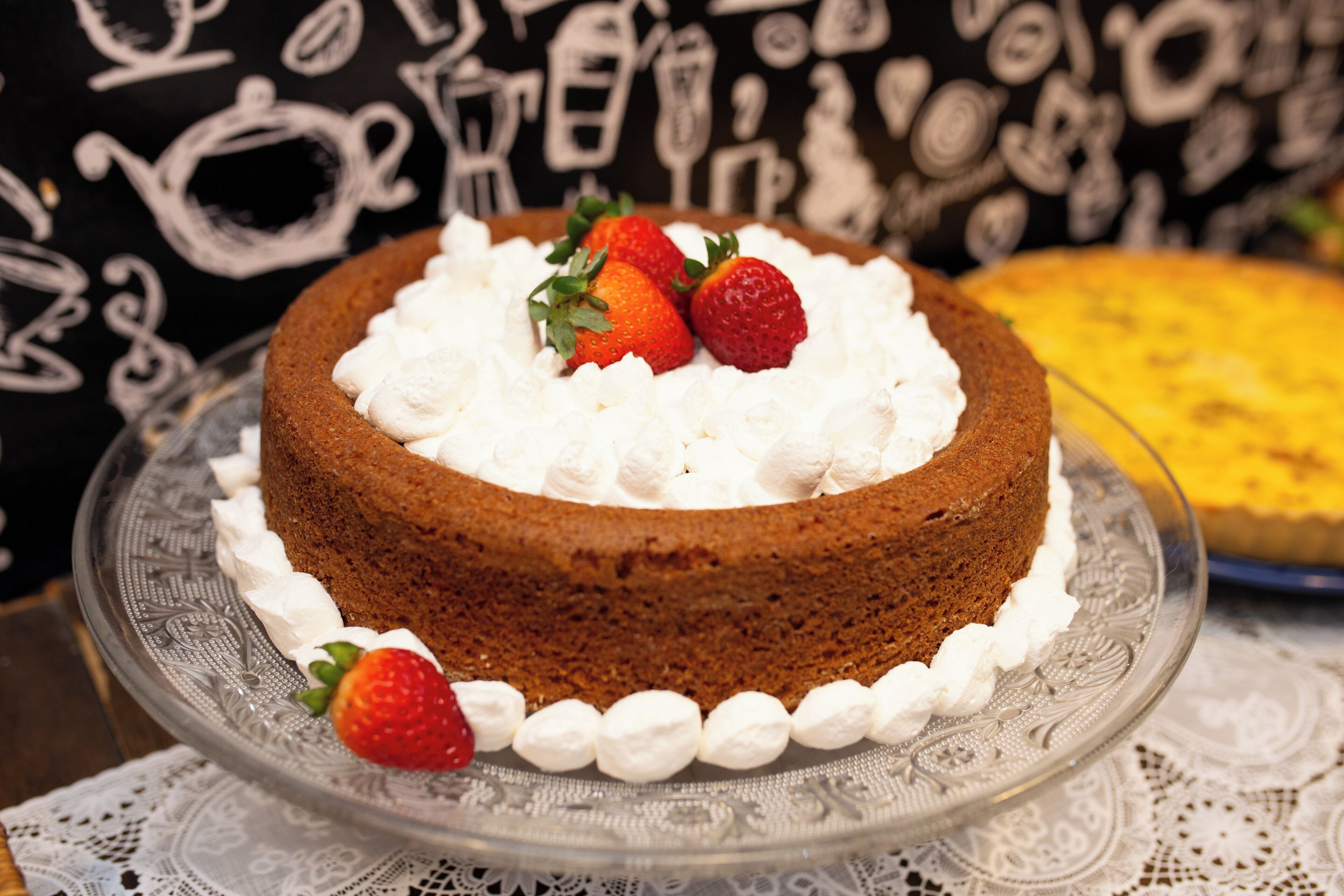Un gâteau décoré de fraises, présenté sur un présentoir à gâteaux en verre.