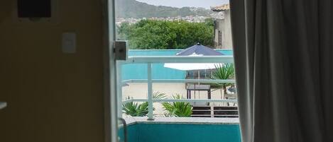 Una habitación con cama, ventana con cortinas y vistas a una piscina y vegetación.