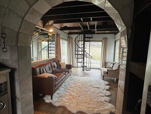 Una sala de estar acogedora con un sofá de cuero, un manto de piel y una escalera en espiral.