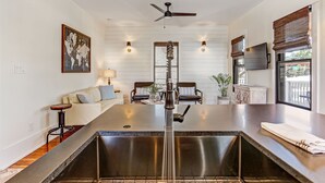 A kitchen with a central island, a dining area with two chairs, a sofa, and a ceiling fan.