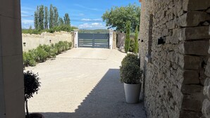A gravel driveway leading to a gated entrance, flanked by stone walls and potted plants. - Villa Rube's (Gordes)