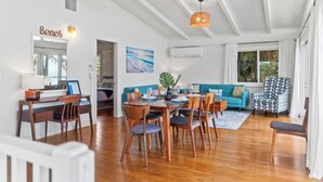 A spacious living area with a wooden dining table, chairs, a sofa, and a ceiling fan. - Surfers Paradise: Ocean View, Walking Distance to Sunset Beach NUC:1990/NUC-2073 (Haleiwa)