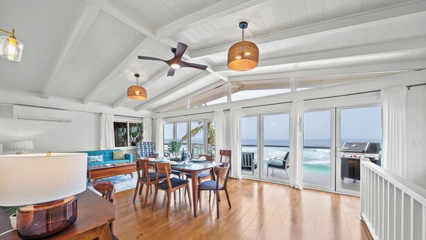 A spacious living area with a dining table, chairs, and a large window overlooking the ocean. - Surfers Paradise: Ocean View, Walking Distance to Sunset Beach NUC:1990/NUC-2073 (Haleiwa)