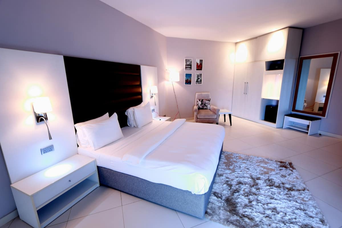 A modern bedroom with a large bed, bedside tables, a chair, a wardrobe, and a mirror.