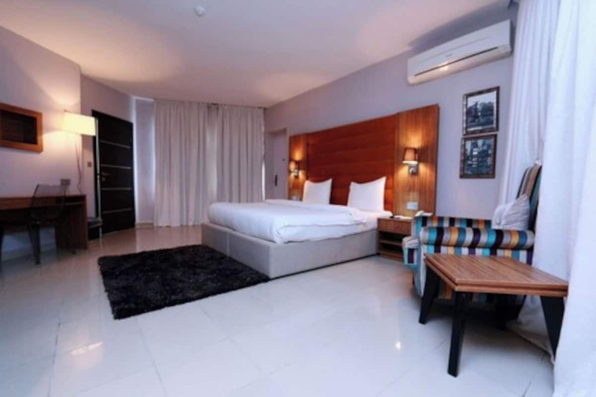 A modern hotel room with a large bed, a sofa, a small table, and a desk.