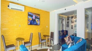 Un área de estar moderna con un muro de ladrillo amarillo, un televisor de pantalla plana y un sofá azul.