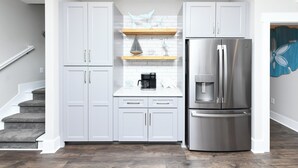A modern kitchen with white cabinets, a stainless steel refrigerator, and a coffee maker on the countertop. - 5 BR Beach House with a Private Pool! Grace's Places "FKA Blessed in Waves" (Surfside Beach)