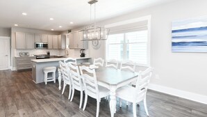 A modern kitchen with white cabinetry, a central island, and a dining area with white chairs. - 5 BR Beach House with a Private Pool! Grace's Places "FKA Blessed in Waves" (Surfside Beach)