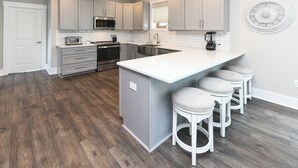 A modern kitchen with grey cabinets, a white countertop, and a central island with bar stools. - 5 BR Beach House with a Private Pool! Grace's Places "FKA Blessed in Waves" (Surfside Beach)