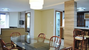 Una sala de estar moderna con una mesa de comedor de vidrio, sillas de madera, un sofá y una cocina con un muro decorativo de madera.