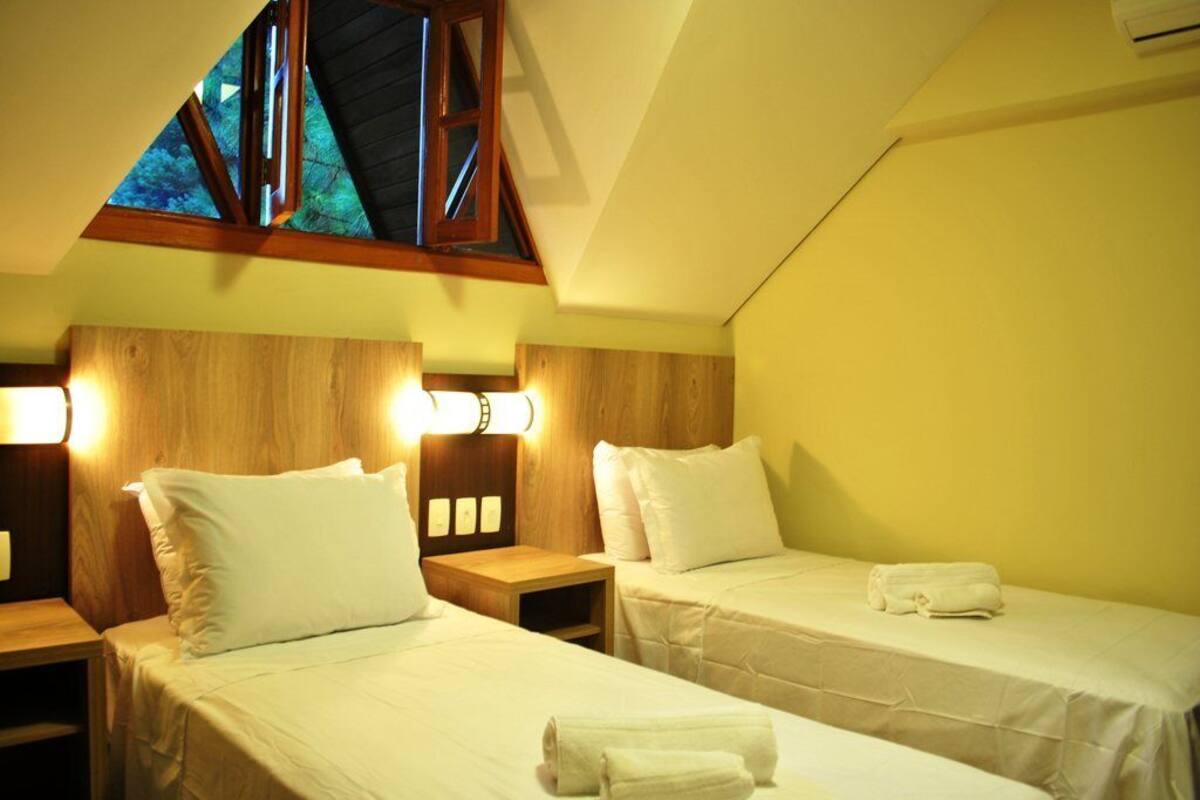 Quarto de hotel com duas camas, cabeceiras de madeira, abajures e um claraboia.