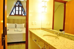 Habitación de hotel con cama, baño con lavamanos y espejo, y ventana con marco de madera.