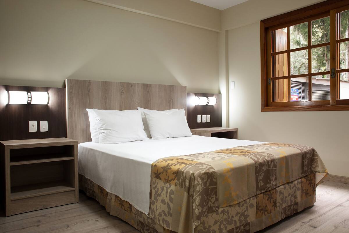 Quarto com cama, mesas de cabeceira e janela.