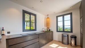 A modern kitchen with a large island, two windows with views, and a hanging light fixture. - Nice villa completely renovated (Gassin)