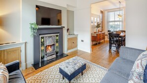 Ein Wohnzimmer mit Kamin, einer Couch, einem gemusterten Teppich und einem Essbereich mit Tisch und Stühlen.