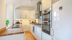 Eine moderne Küche mit weißen Schränken, Edelstahlgeräten, einer Holz Arbeitsplatte und einem eingebauten Backofen.