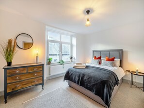 A bedroom with a bed, dresser, window, and bedside table.