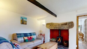 Una sala de estar acogedora con un sofá, una mesa de centro de madera, una chimenea con leña y un estante rústico de piedra.